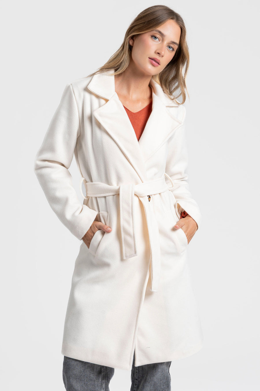 Manteau blanc croisé avec ceinture nouée sur un haut orange, vue de trois quarts