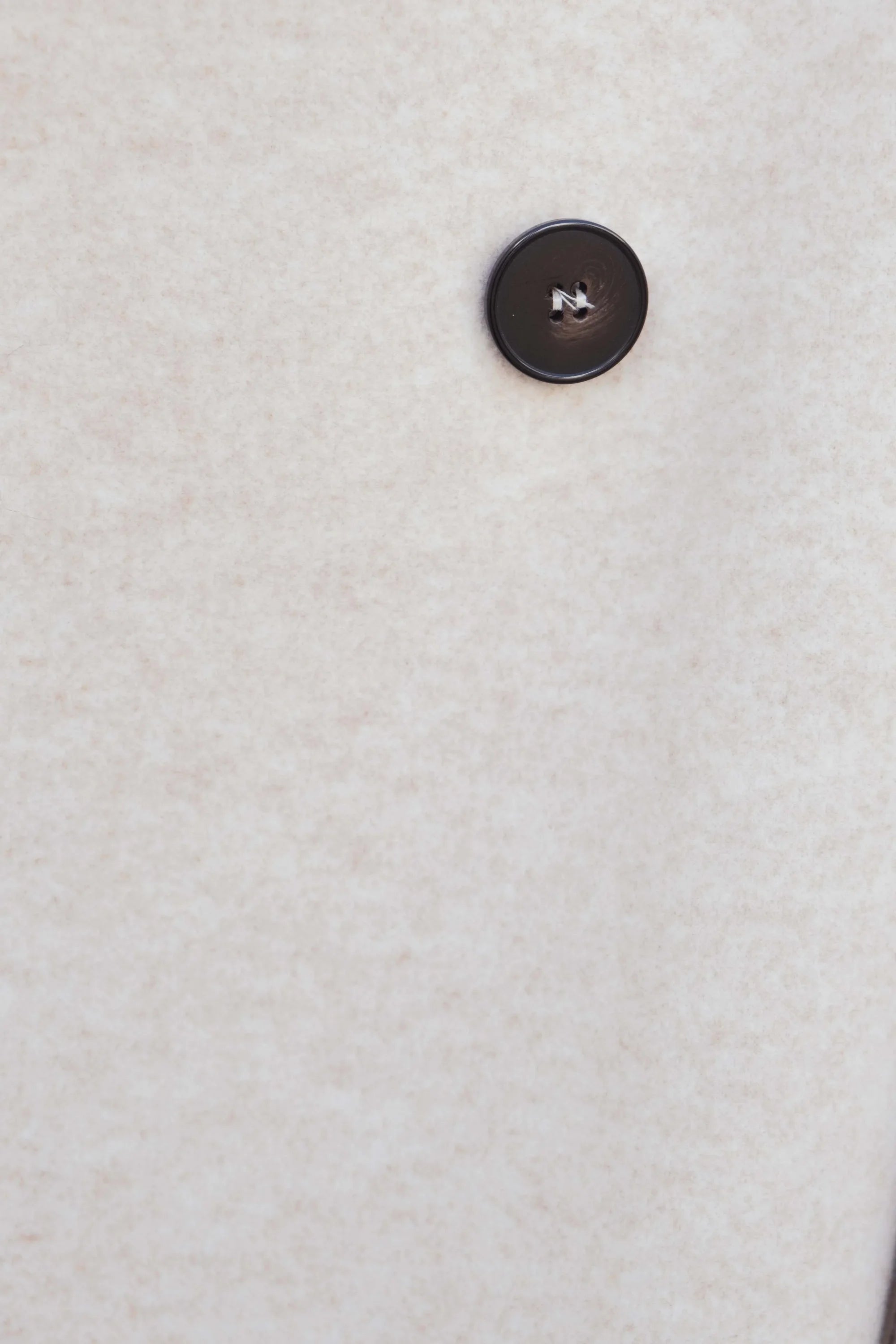 Bouton marron foncé à quatre trous sur tissu clair, idéal pour manteau croisé femme