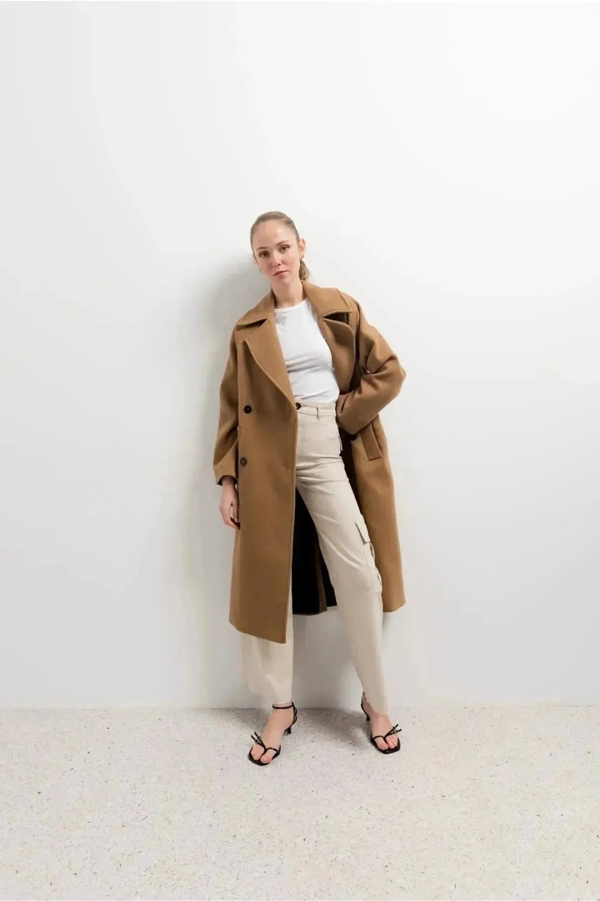 Femme élégante posant avec un manteau long en laine camel, un incontournable de la saison hivernale, le manteau femme hiver long.