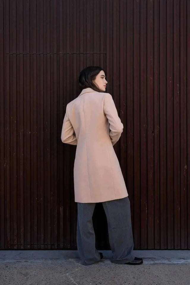 Vue arrière d'un manteau beige femme long élégant sur un modèle, avec une ambiance moderne.