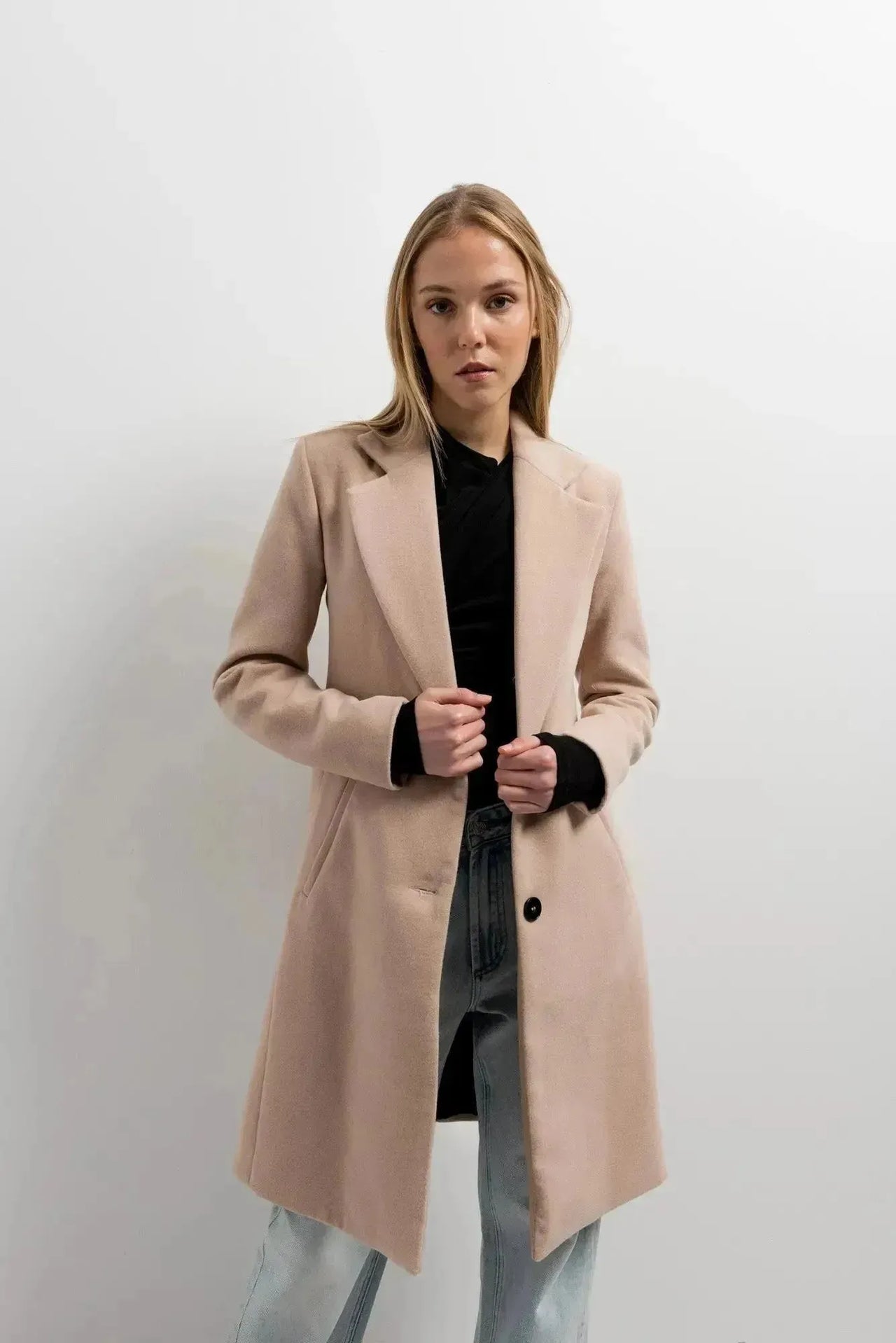 Manteau beige femme long élégant sur un modèle avec un ensemble décontracté, ajoutant une touche de chic à la garde-robe.