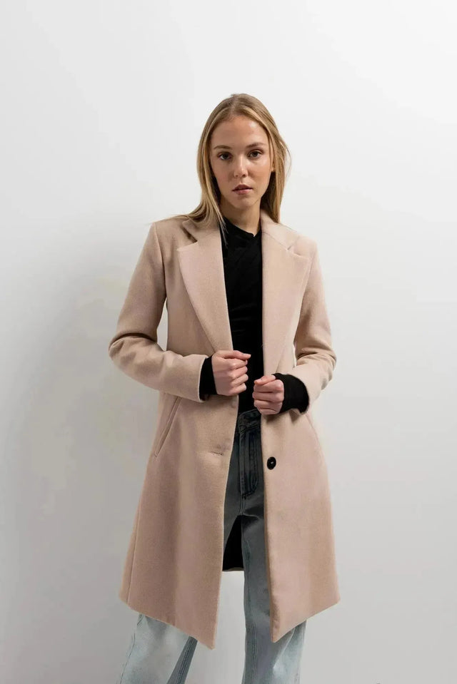 Manteau beige femme long élégant sur un modèle avec un ensemble décontracté, ajoutant une touche de chic à la garde-robe.