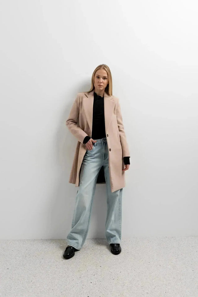 Manteau beige femme long élégant montré par un modèle avec look décontracté, idéal pour les journées fraîches.