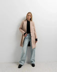 Manteau beige femme long élégant montré par un modèle avec look décontracté, idéal pour les journées fraîches.