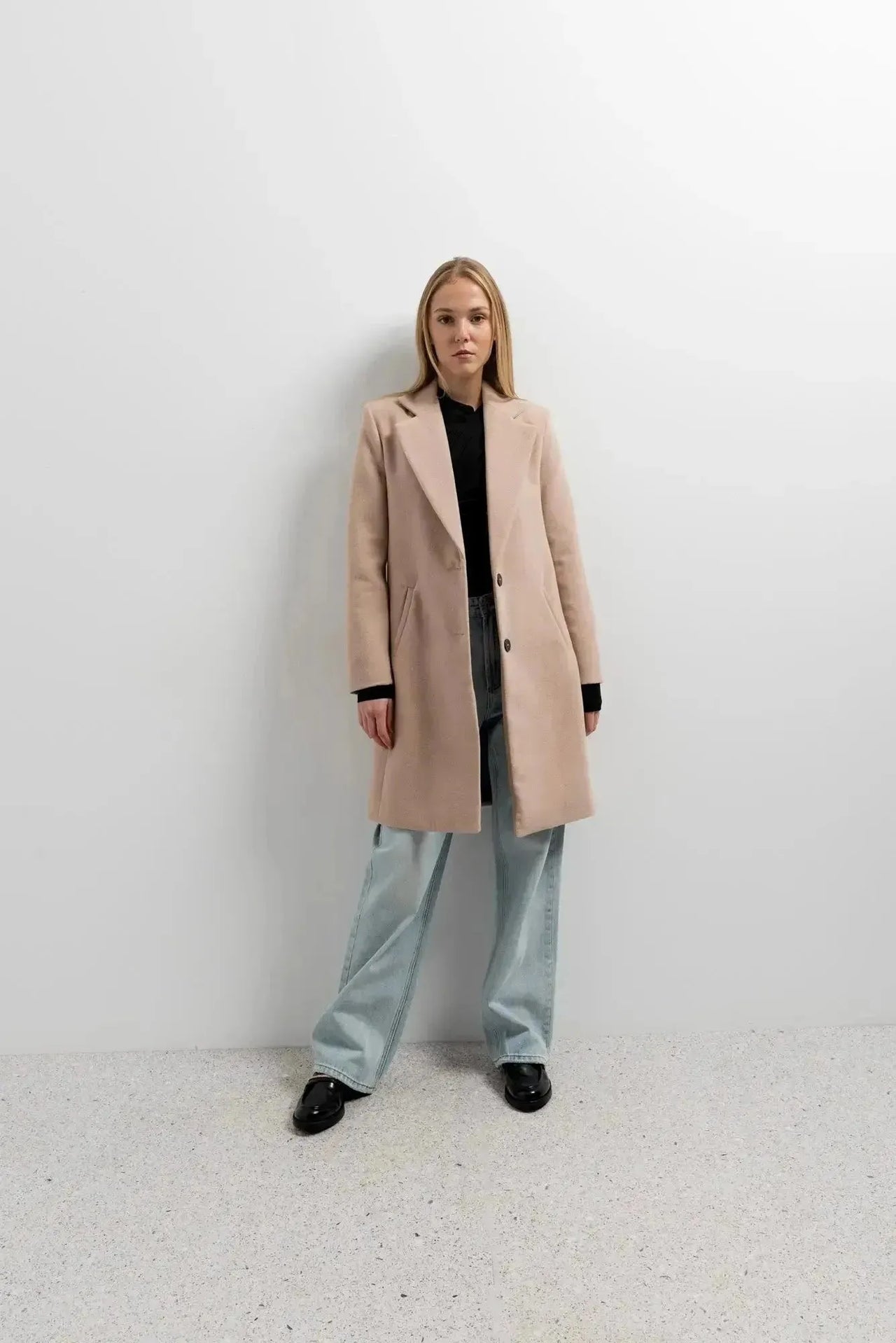 Modèle en manteau beige femme long élégant avec chemise noire et pantalon large, combinaison parfaite pour l'hiver.