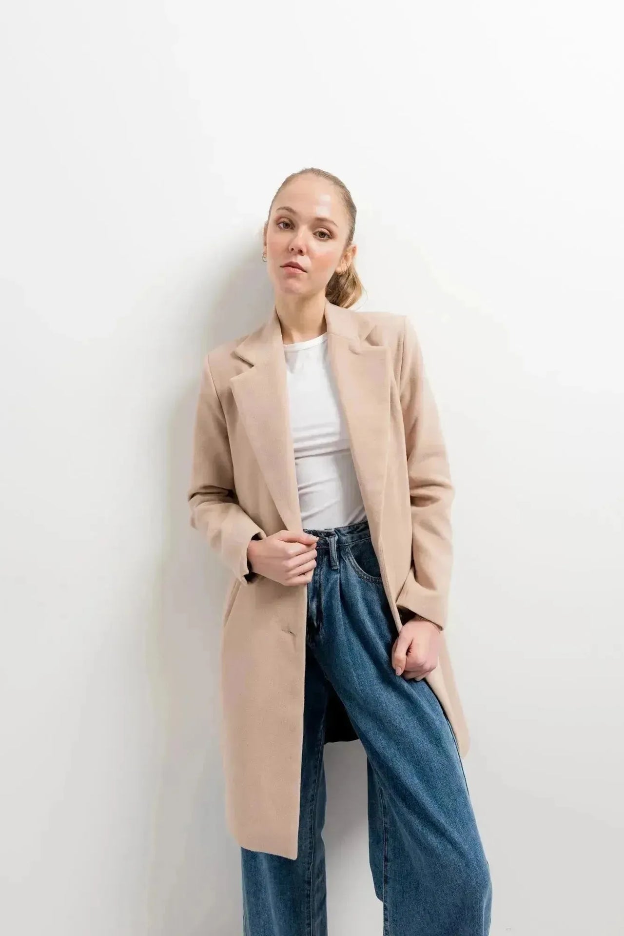 Manteau beige femme long élégant stylé sur un modèle avec un haut blanc et un pantalon en jeans, parfait pour un look décontracté.