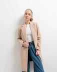 Manteau beige femme long élégant stylé sur un modèle avec un haut blanc et un pantalon en jeans, parfait pour un look décontracté.