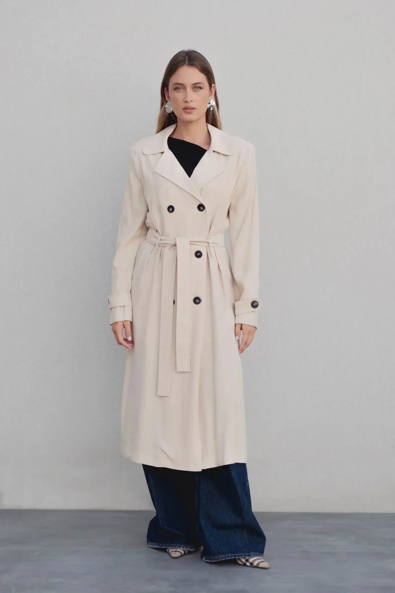 Femme posant avec un manteau trench femme fluide long beige, ceinturé, créant un look chic inspiré de la mode.