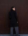 Manteau Long Chaud Femme: Vue arrière d'une femme en manteau noir, soulignant la coupe moderne et l'élégance adaptée à l'hiver.