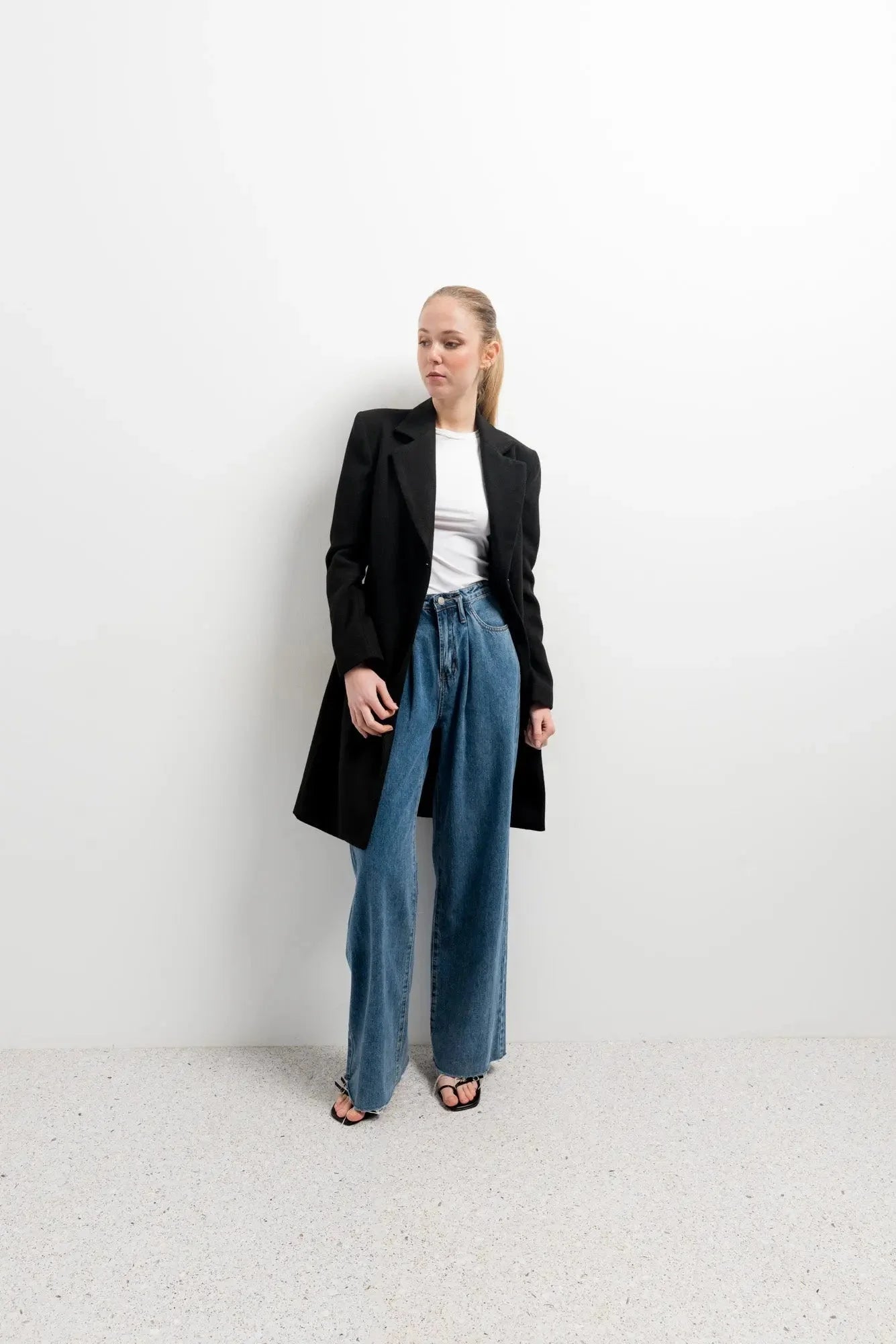 Femme portant un manteau noir avec revers en col, crop top blanc et jeans larges