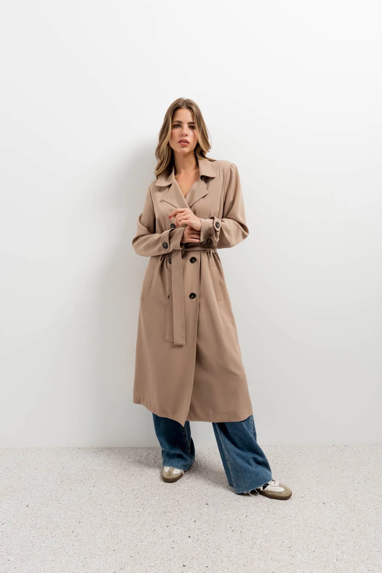Manteau trench oversize long marron clair porté avec jeans larges et chaussures argentées