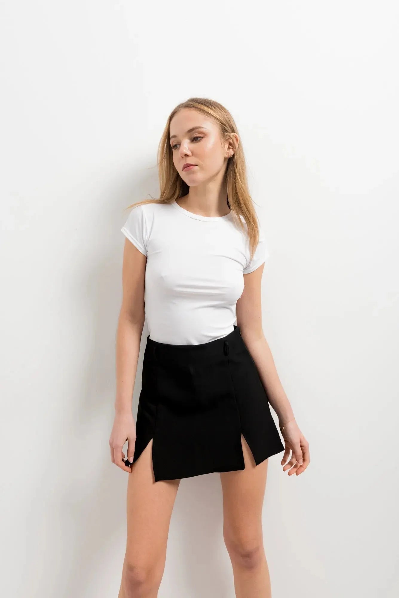 Femme en mini jupe noir fendue, affichant un look élégant, portant un haut blanc et une jupe avec deux fentes.