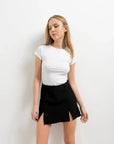 Femme en mini jupe noir fendue, affichant un look élégant, portant un haut blanc et une jupe avec deux fentes.