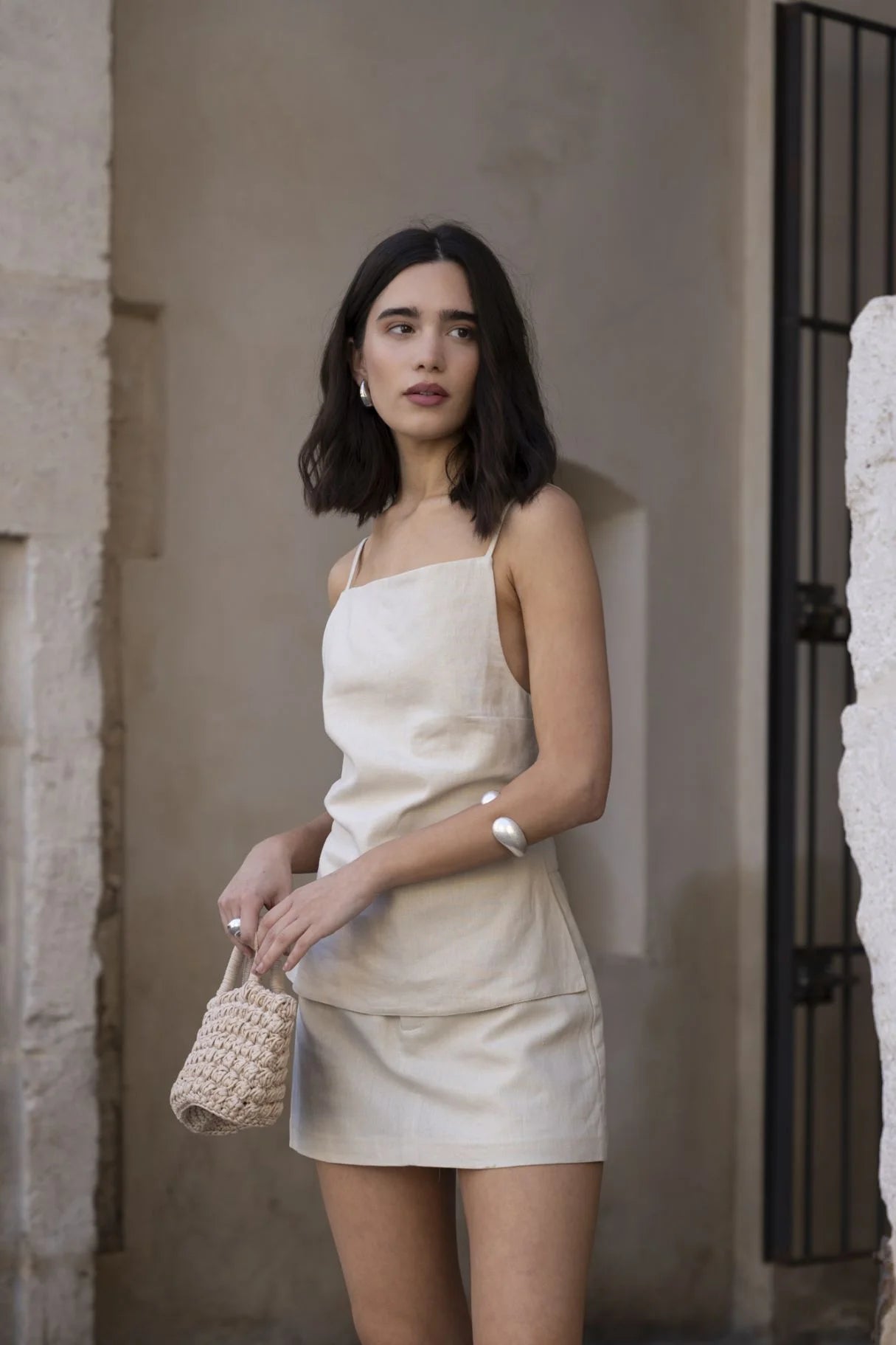 Modèle portant une mini jupe short en lin naturel 100% léger et respirant, taille haute chic minimaliste, se tenant avec un sac en paille.