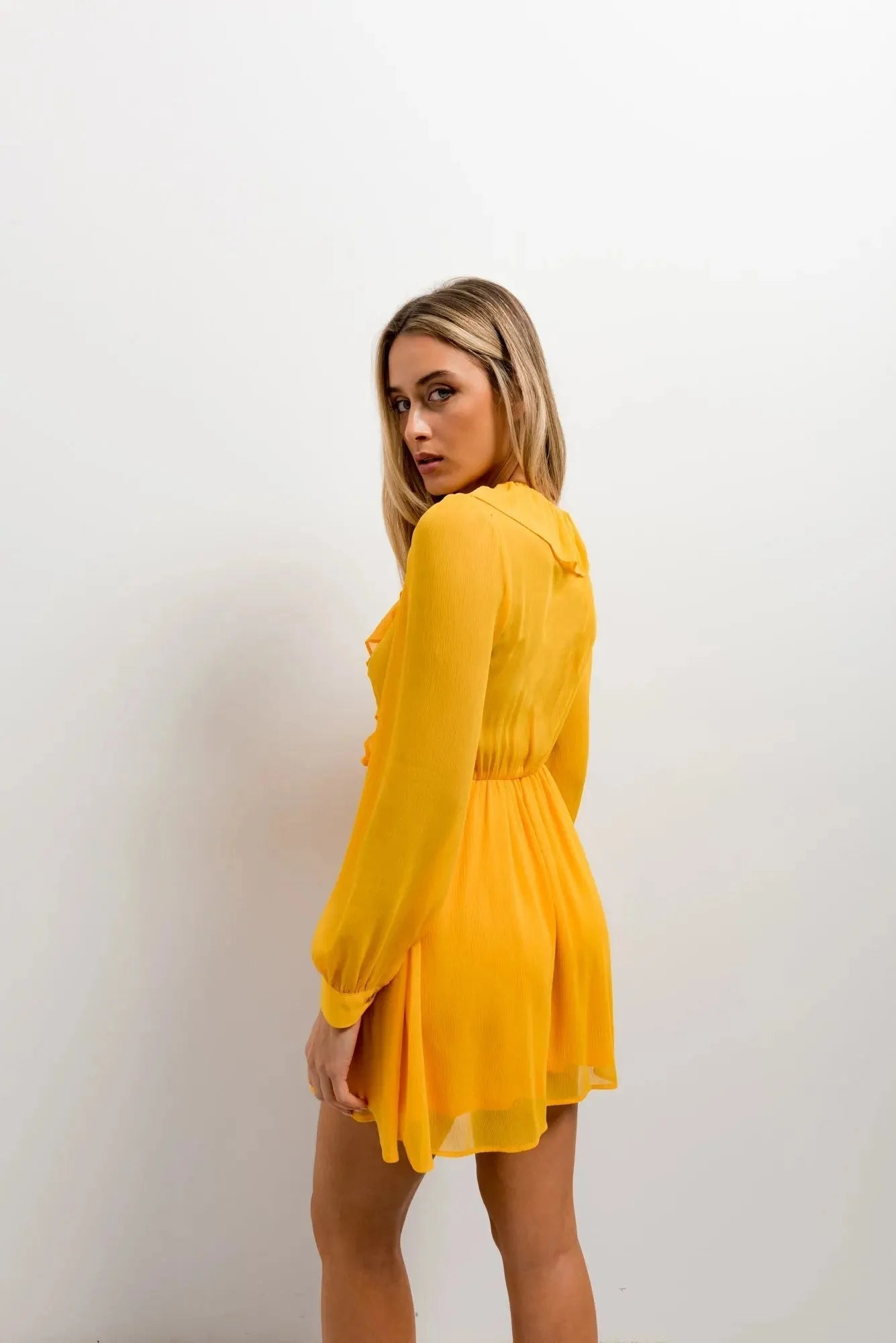 Vue arrière d'un modèle dans la Mini Robe Courte Jaune à Volants, illustrant la coupe élégante et le design versatile de cette robe courte jaune.