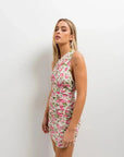 Modèle portant une mini robe moulante froncée à imprimé floral rose, vue de profil, mettant en avant les détails de la coupe cintrée.