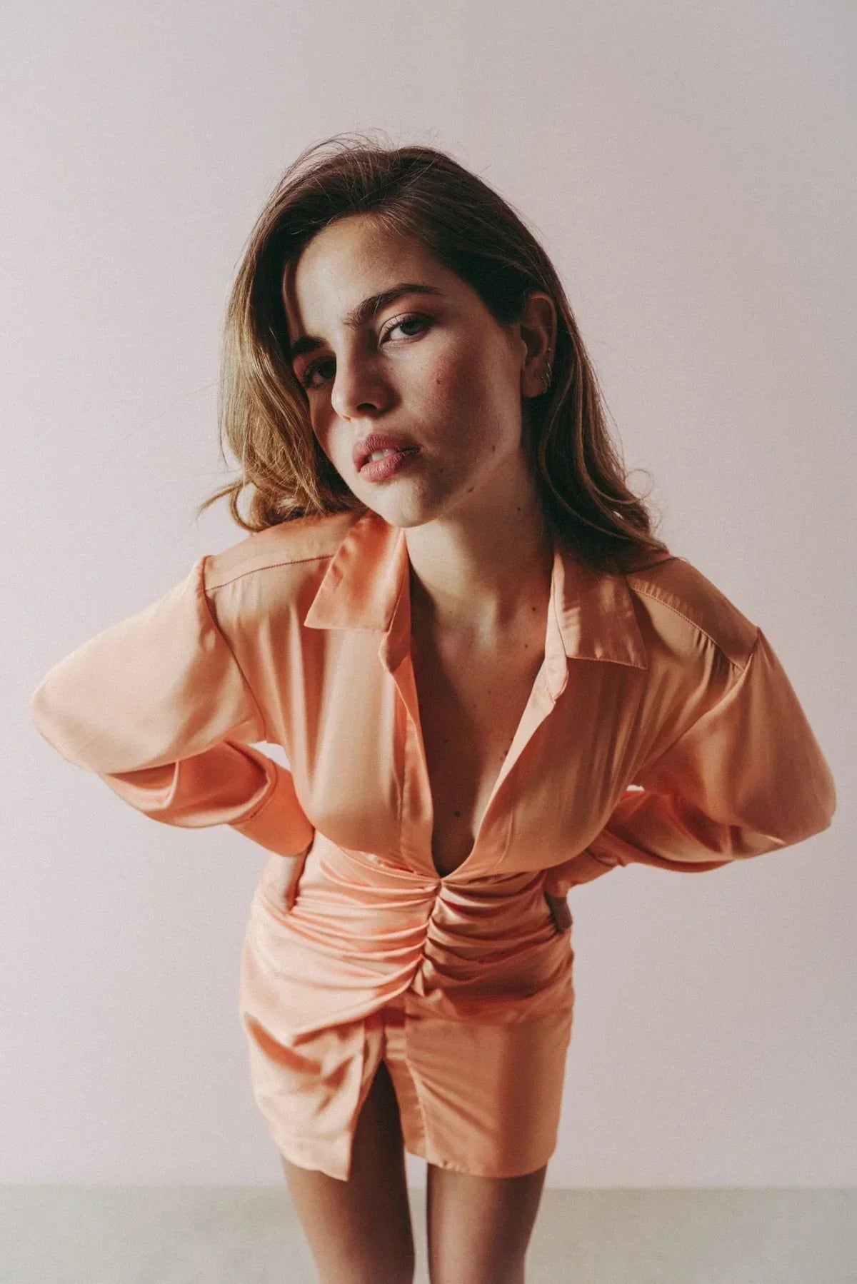 Femme en robe satinée orange pêche manches longues avec col et détails ruchés