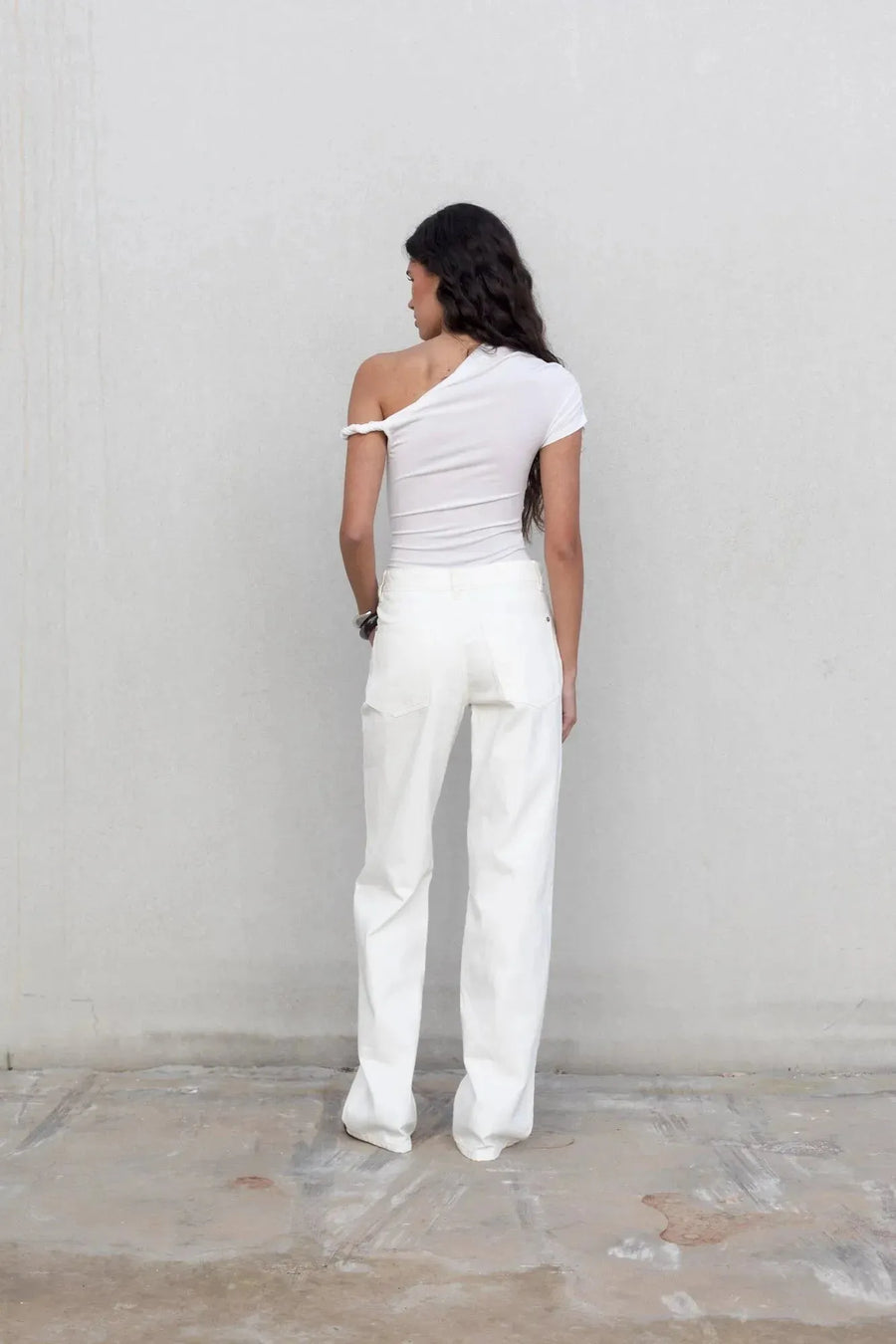 Vue arrière d'un mannequin en pantalon blanc femme à jambe large, révèle une silhouette élégante avec un top blanc.