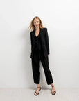 Femme portant un pantalon court plissé taille basse noir avec un blazer, mettant en valeur le pantalon court noir femme dans une tenue chic.