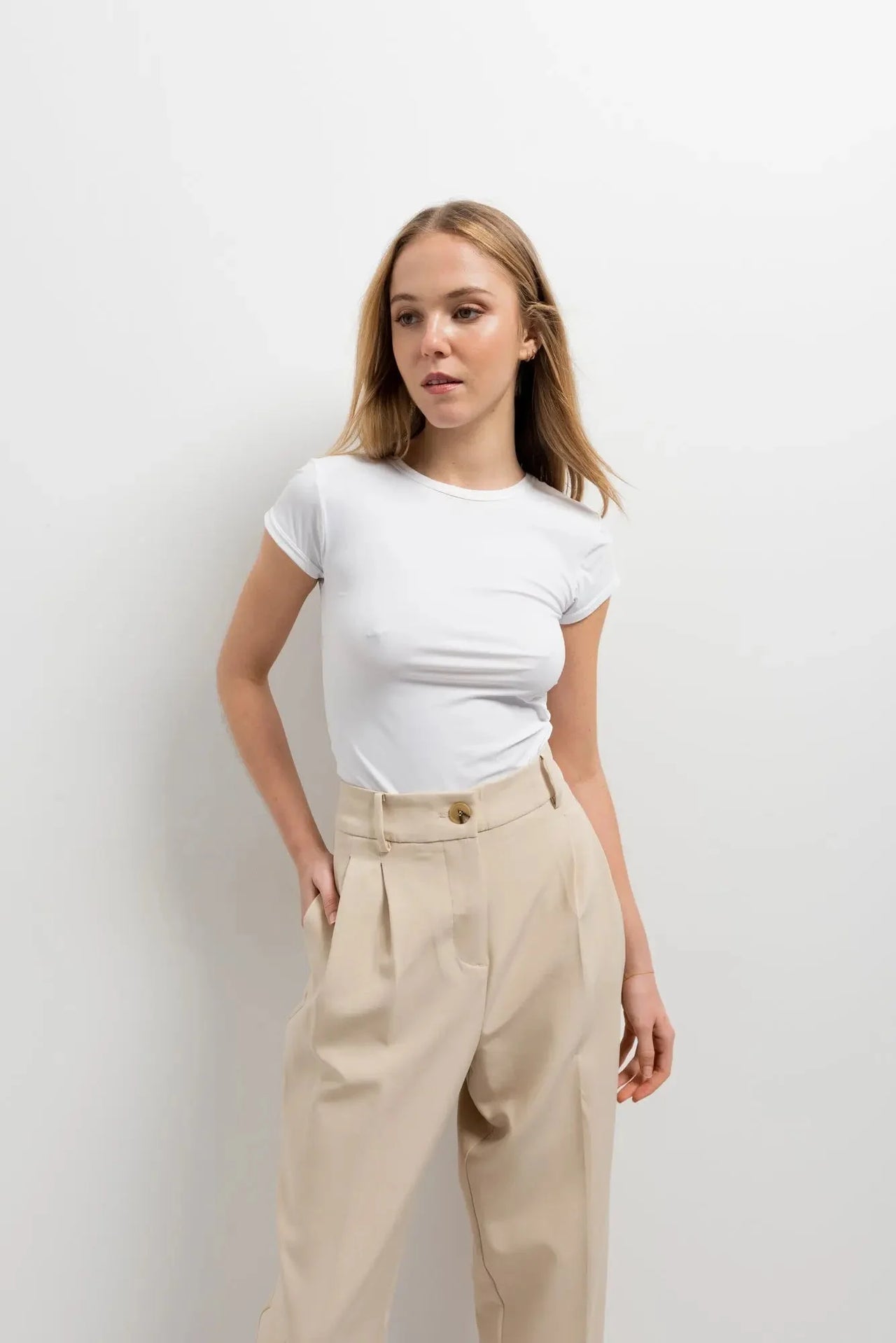 Femme posant en t-shirt blanc avec un pantalon court plissé taille basse beige, mettant en avant la versatile élégance du pantalon court noir femme.