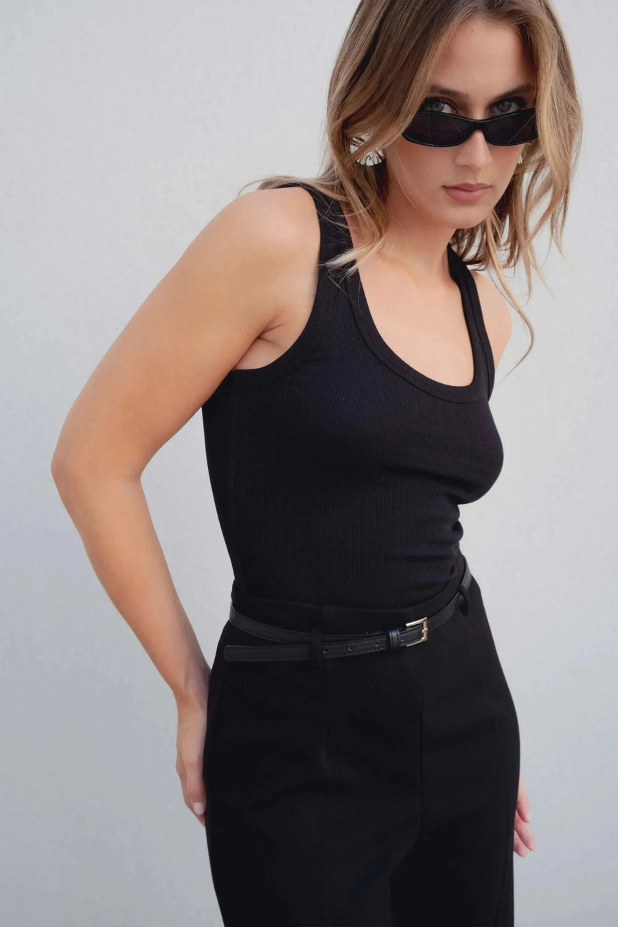 Gros plan sur une femme portant un pantalon culotte taille haute jambe large noir boucle métallique, le haut noir et la ceinture ajoutent une touche moderne.
