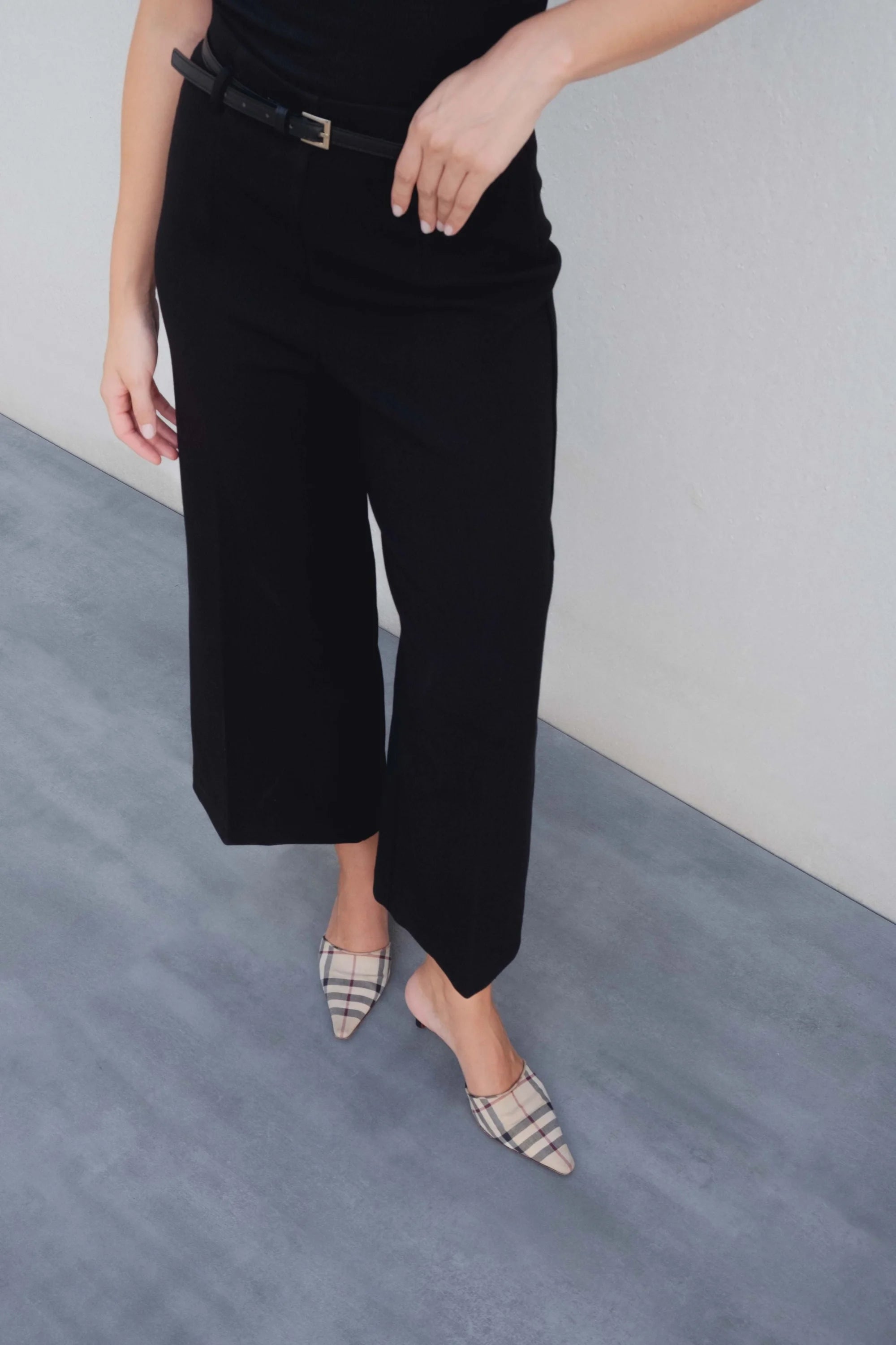 Détail des jambes d'une femme en pantalon culotte taille haute jambe large noir boucle métallique et des chaussures à motif, combiné avec un haut noir.