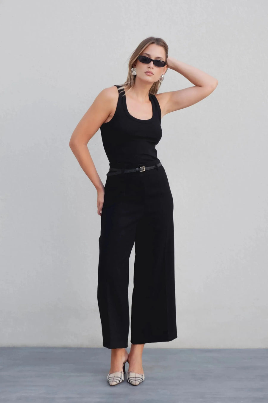 Femme en pose avec un pantalon culotte taille haute jambe large noir boucle métallique, mettant en valeur son style élégant avec des lunettes de soleil.