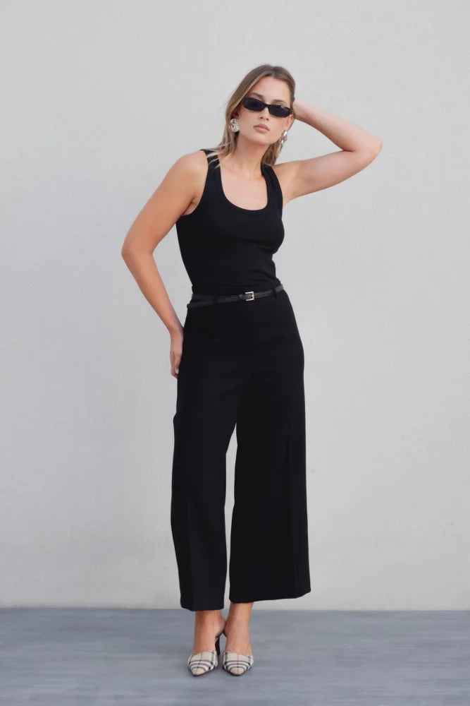 Femme en pose avec un pantalon culotte taille haute jambe large noir boucle métallique, mettant en valeur son style élégant avec des lunettes de soleil.