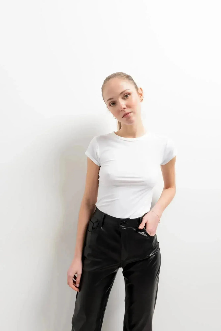 Femme posant avec le Pantalon Effet Cuir Noir Élégant et un top blanc, parfait pour un look décontracté. Le pantalon imitation cuir femme idéal pour toutes les occasions.