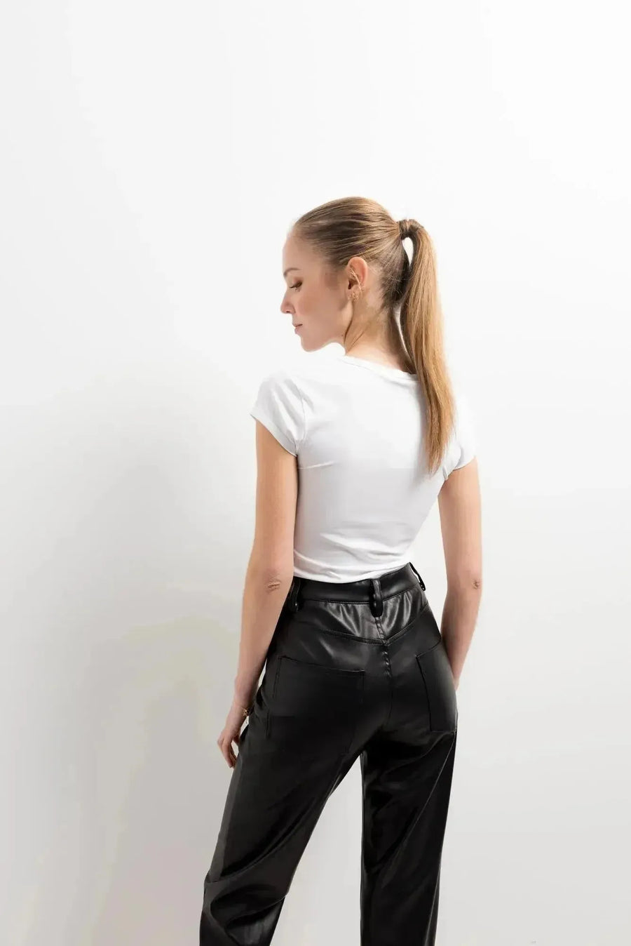 Femme de dos en Pantalon Effet Cuir Noir Élégant avec un haut blanc, montrant le style moderne et épuré. Un choix préféré pour le pantalon imitation cuir femme.
