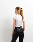 Femme de dos en Pantalon Effet Cuir Noir Élégant avec un haut blanc, montrant le style moderne et épuré. Un choix préféré pour le pantalon imitation cuir femme.