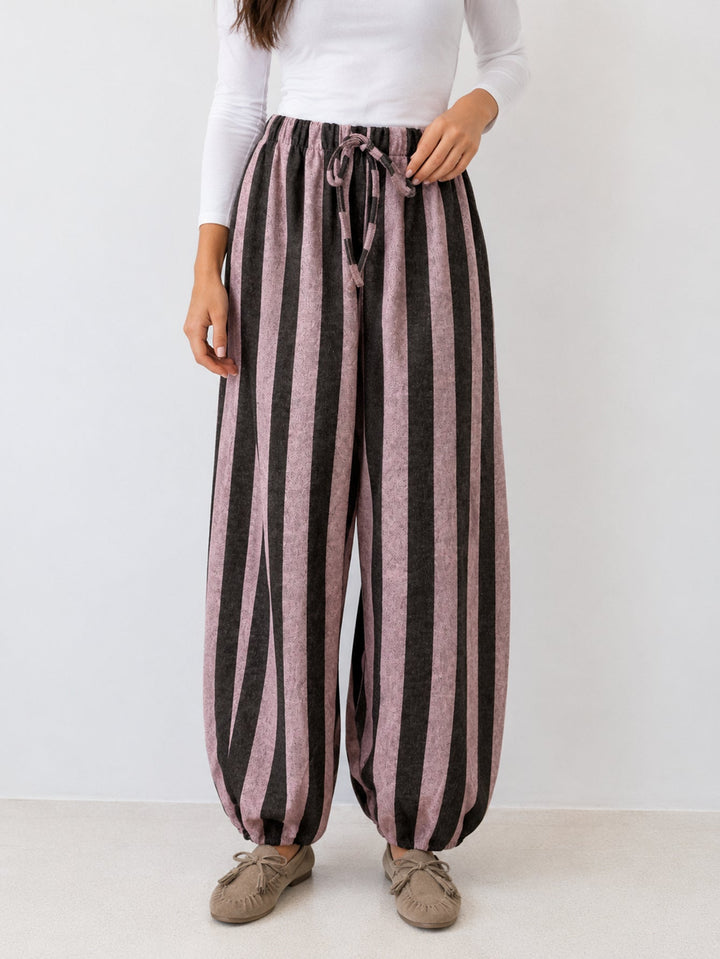 Pantalon ample à rayures verticales roses et foncées, porté de face, avec lien noué à la taille.