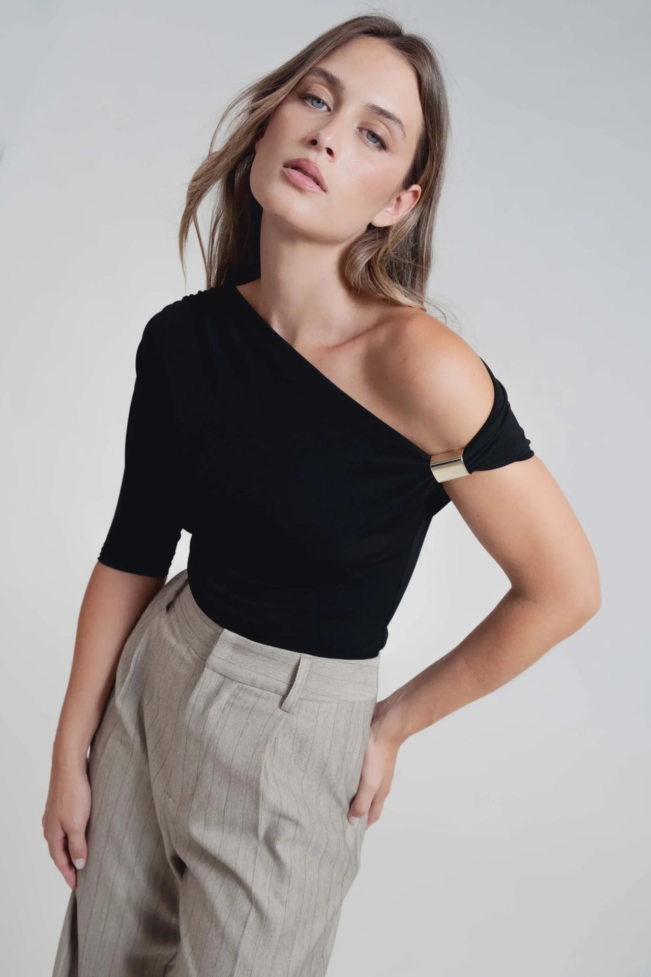 Modèle féminin présentant un haut noir asymétrique et un pantalon fluide à rayures, mettant en valeur le pantalon fluide femme taille haute.