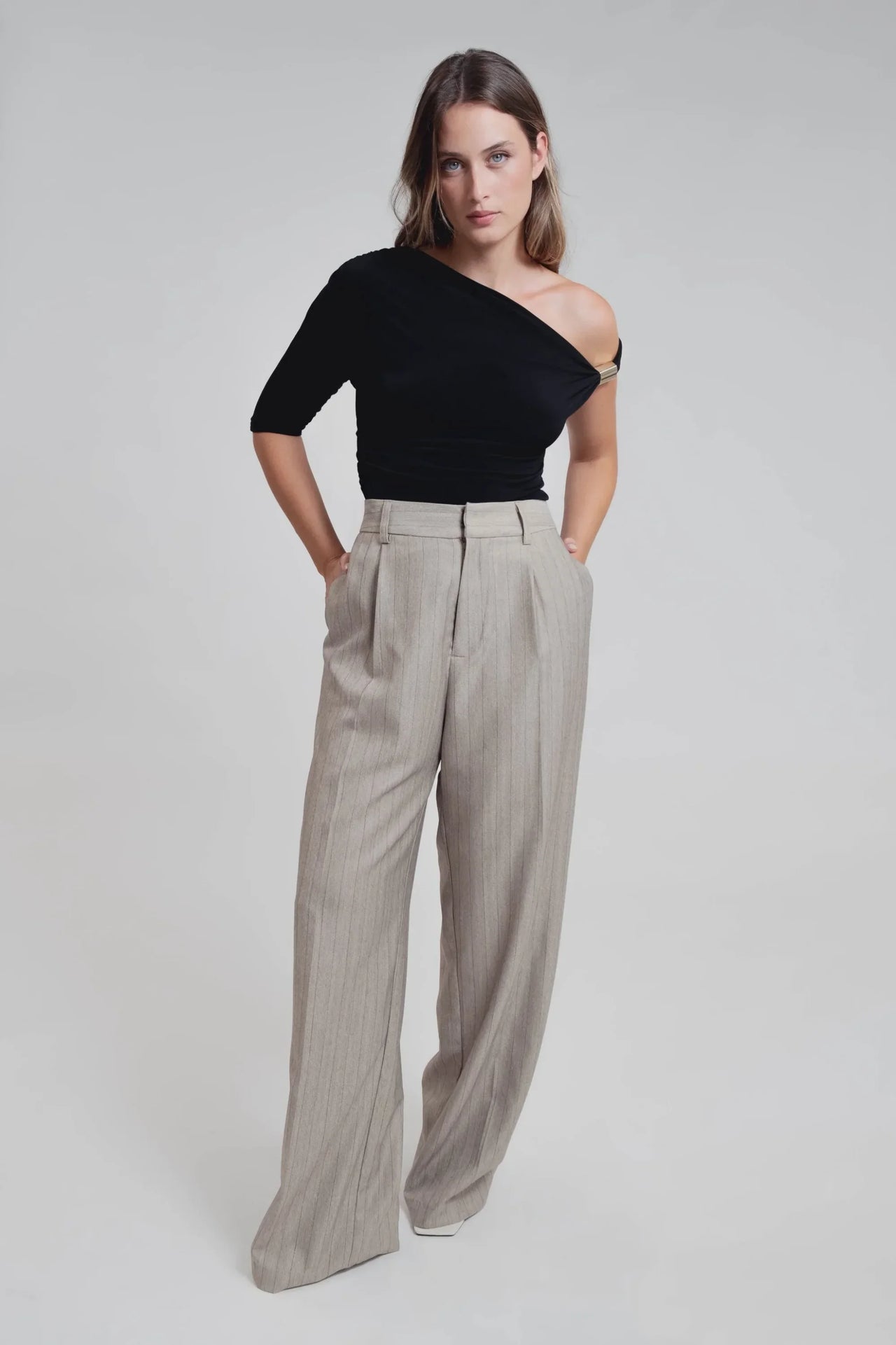Femme en pose élégante avec un haut noir et un pantalon fluide à rayures, mettant l'accent sur le pantalon fluide femme taille haute.