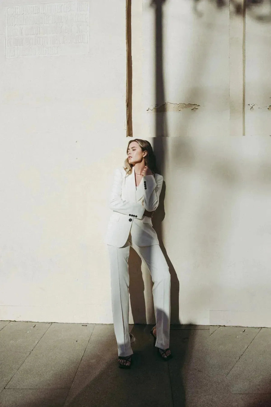 Femme en pantalon habillé femme écru lumineux et blazer assorti, posée contre un mur, affichant un look professionnel et moderne.