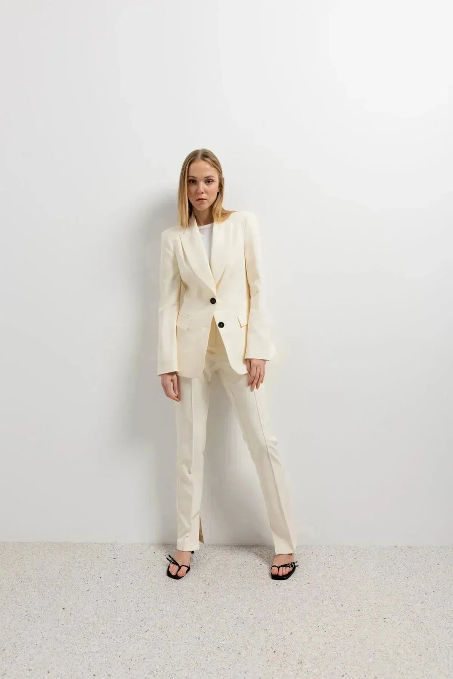 Femme habillée avec un pantalon habillé femme écru lumineux et blazer, style élégant, se tenant debout dans un environnement minimaliste.