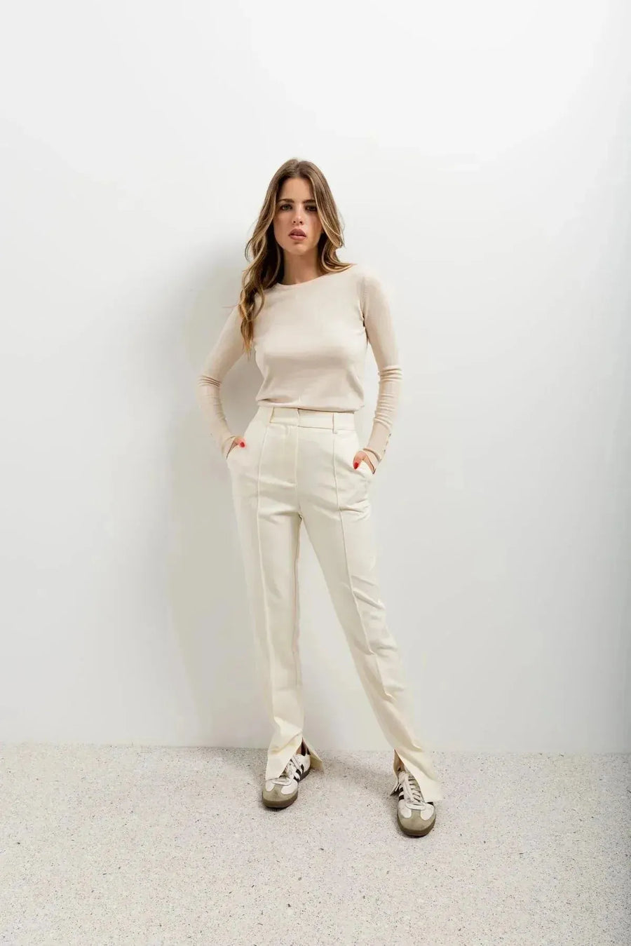 Femme avec un style casual chic, portant un pantalon habillé femme écru lumineux et un pull beige, mains dans les poches.