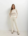 Femme avec un style casual chic, portant un pantalon habillé femme écru lumineux et un pull beige, mains dans les poches.