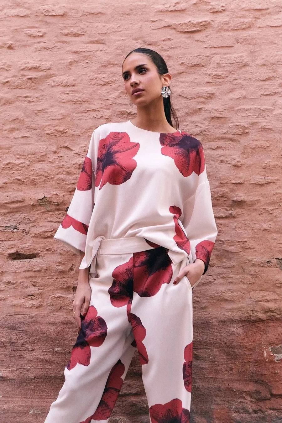Femme posant avec élégance dans un pantalon habillé fluide – Coupe droite moderne – Blanc à fleurs rouges – Matière légère, mettant en avant le pantalon motif femme.