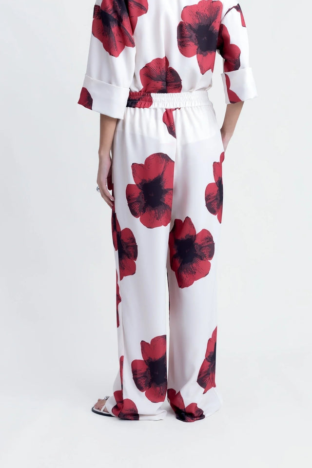 Vue arrière d'une femme dans un pantalon habillé fluide – Coupe droite moderne – Blanc à fleurs rouges – Matière légère, révélant le pantalon motif femme.
