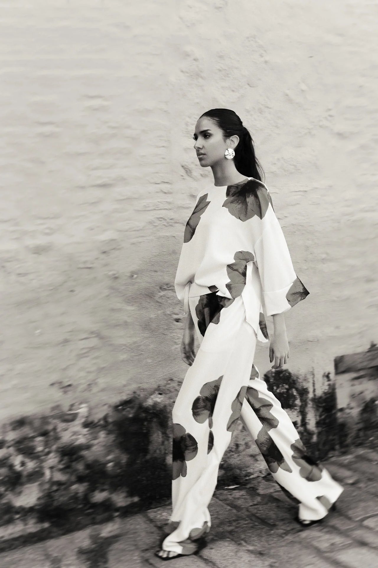 Femme marchant avec assurance dans un pantalon habillé fluide – Coupe droite moderne – Blanc à fleurs rouges – Matière légère, illustrant le style du pantalon motif femme.