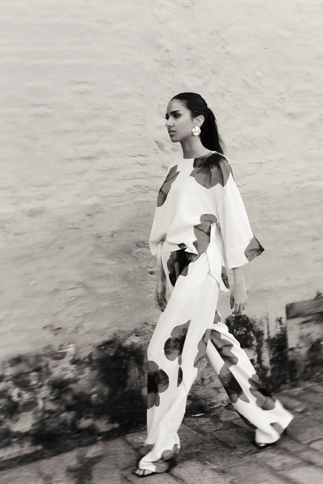 Femme marchant avec assurance dans un pantalon habillé fluide – Coupe droite moderne – Blanc à fleurs rouges – Matière légère, illustrant le style du pantalon motif femme.