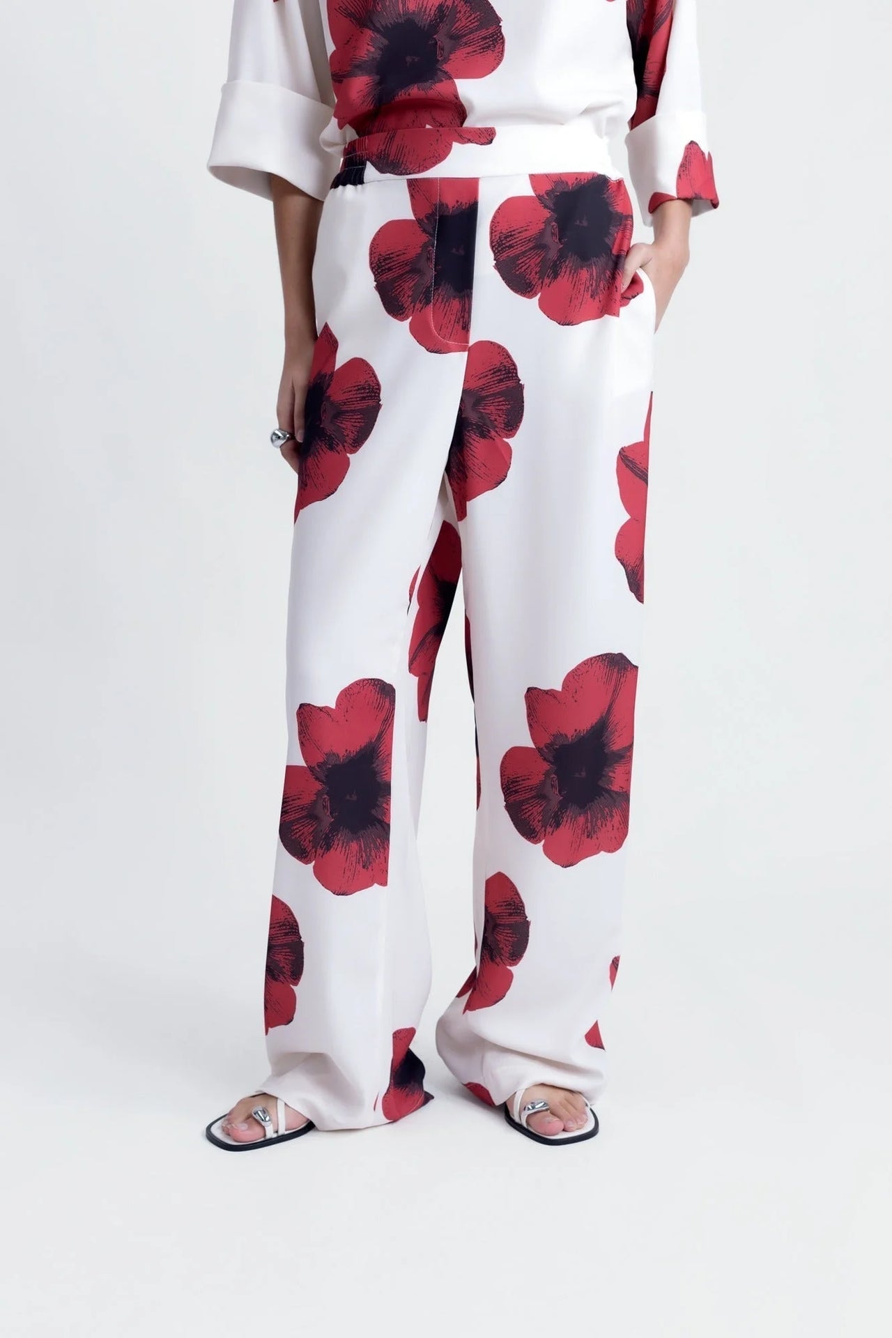 Détail du bas d'un pantalon habillé fluide – Coupe droite moderne – Blanc à fleurs rouges – Matière légère, représentant le pantalon motif femme.