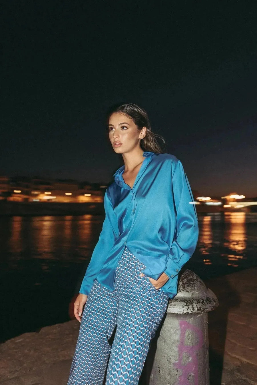 Femme portant un pantalon imprimé taille haute à jambe large, stylé avec une chemise bleue, mise en avant le pantalon motif femme au bord d'une rivière.