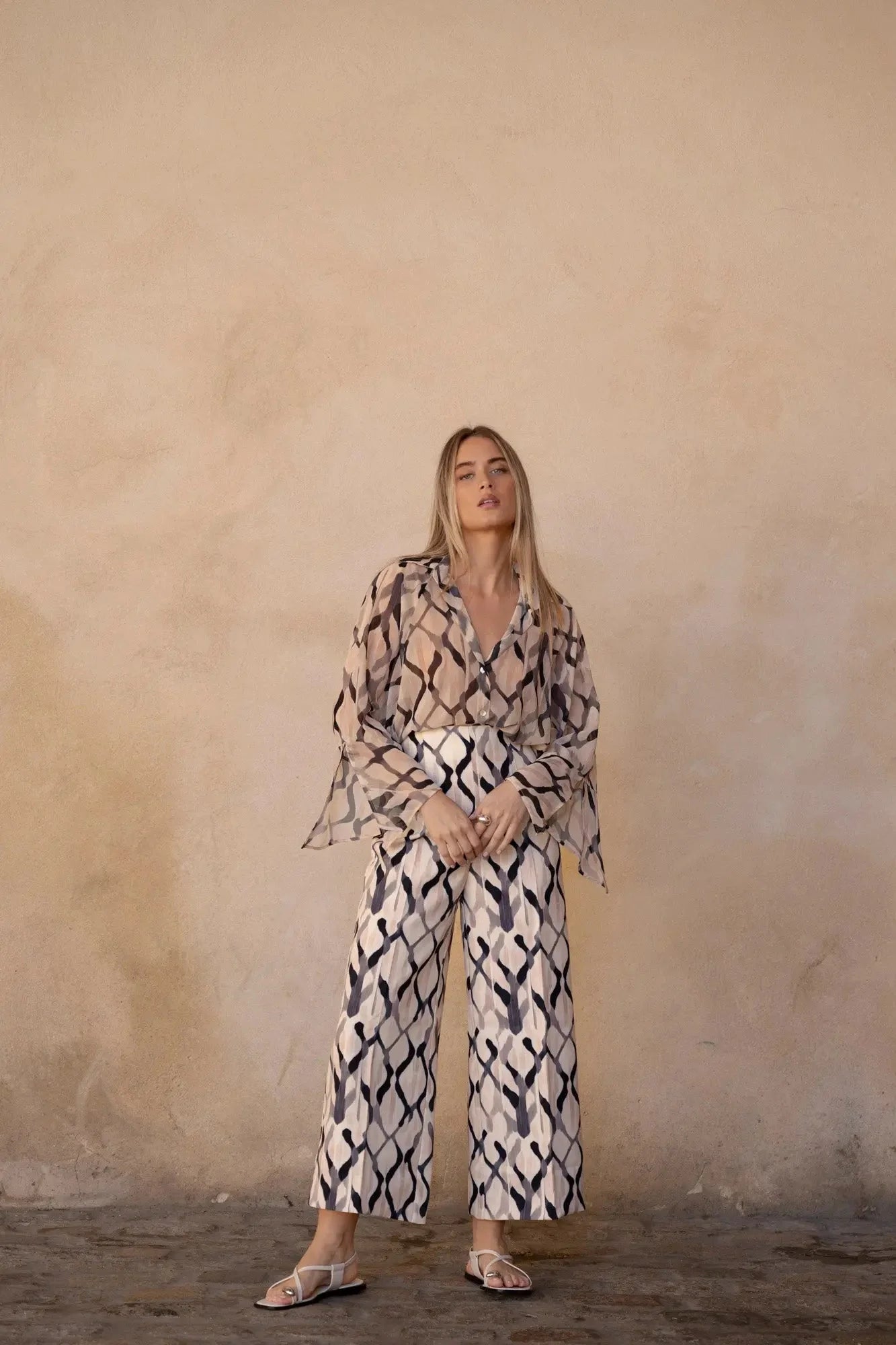Femme portant un pantalon imprimé culotte palazzo, blouse transparente et sandales plates