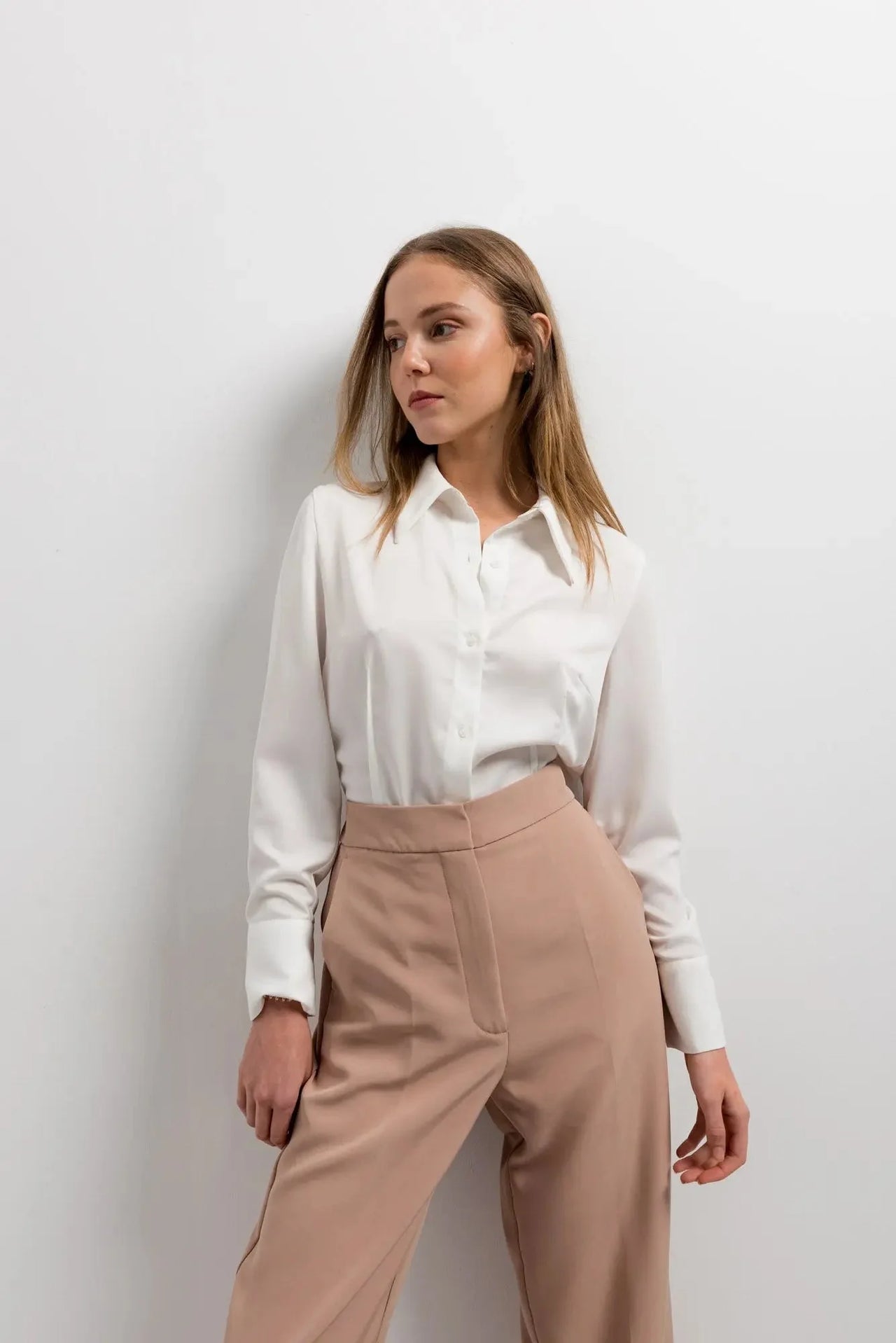 Femme dans un pantalon femme pince à revers, avec une chemise blanche, montrant une pose confiante.