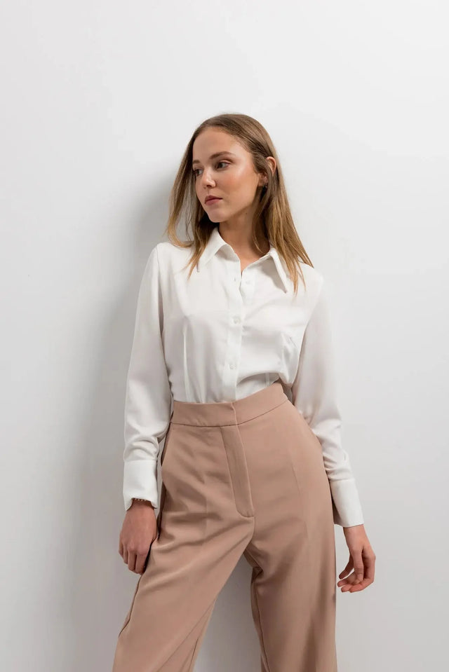 Femme dans un pantalon femme pince à revers, avec une chemise blanche, montrant une pose confiante.