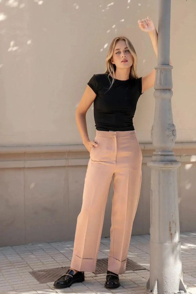 Pantalon femme pince à revers porté par une femme en t-shirt noir, posant contre un lampadaire sur une rue.