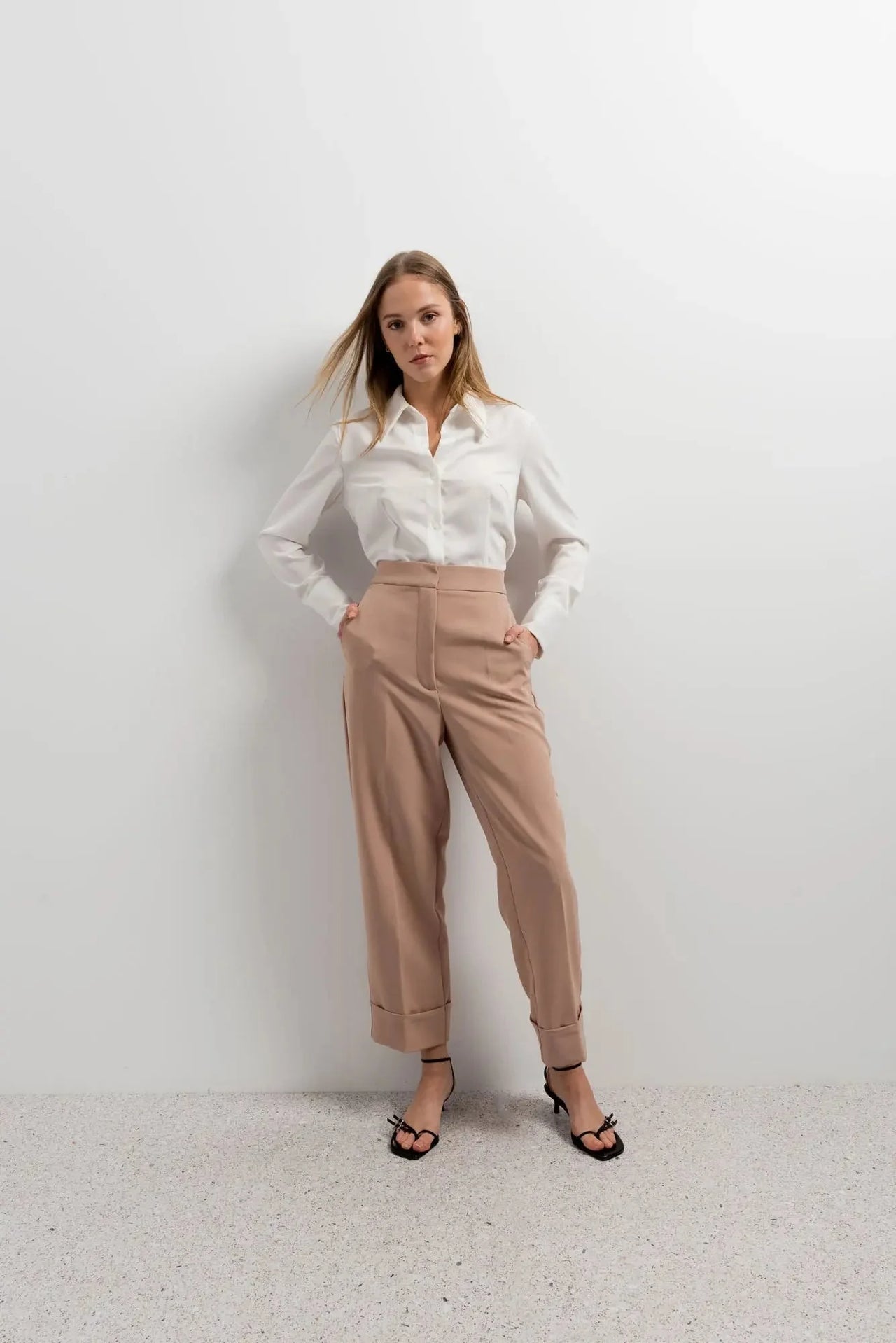 Femme stylée dans un pantalon femme pince à revers et chemise blanche, posant sur fond blanc.