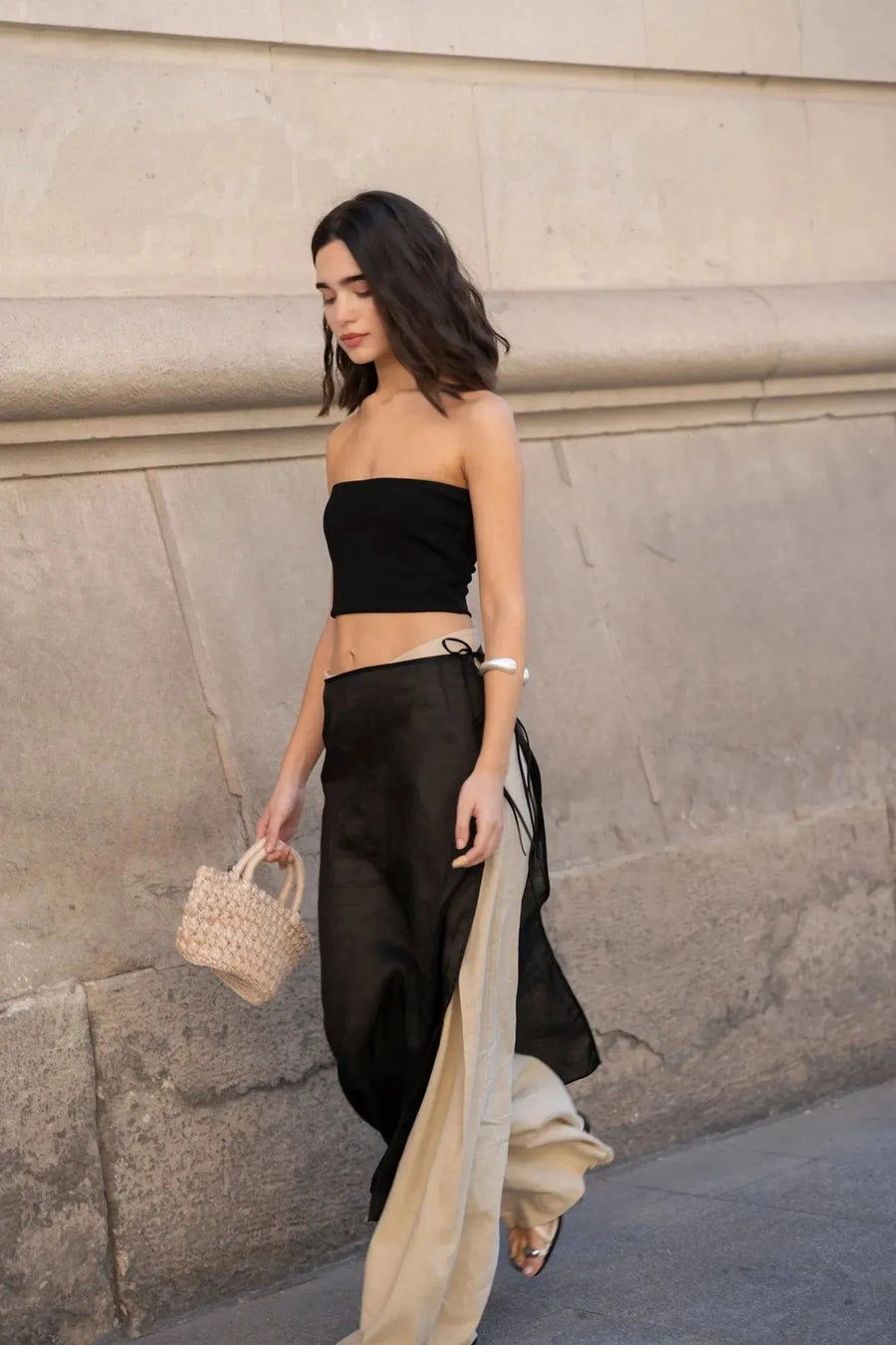 Femme marchant avec un pantalon large et fluide femme beige et un top noir, à côté d'une façade élégante.